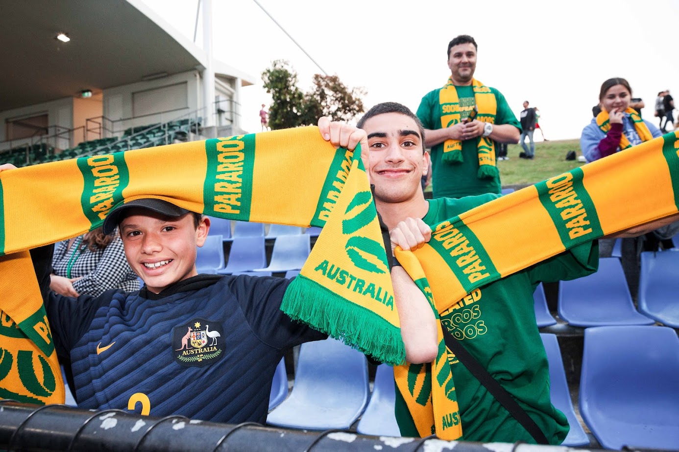 A 13-year-old Kaylan Van Heer (left) holds up a Pararoos scarf in the stands of Cromer Park, Sydney during Pararoos v Canada. A second person alongside him also holds up a scarf.